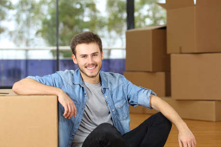 Happy man moving home looking at camera posing sitting on the floor with boxesの写真素材