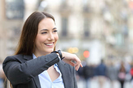 Happy entrepreneur woman dictates voice message on smartwatch looking away in the streetの写真素材