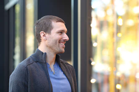 Happy man looking at storefront with lights standing in the street