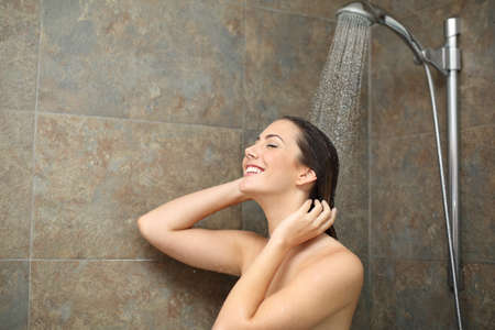 Happy wet woman under water enjoying shower with water falling on head on the bathroomの写真素材