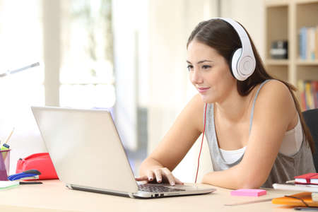 Serious student woman elearning on laptop with headphones sitting on a desk at homeの写真素材