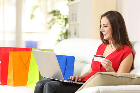 Happy shopper woman paying online with credit card on laptop sitting on a couch at homeの写真素材
