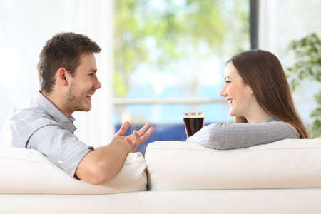 Profile of a happy couple talking and having a coffee in the sofa at homeの写真素材