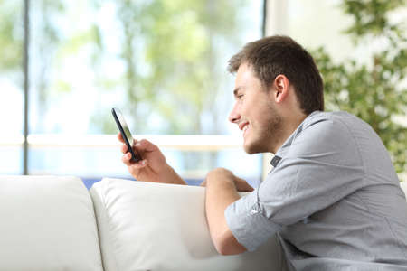 Happy man using smart phone sitting on the sofa in the living room at homeの写真素材