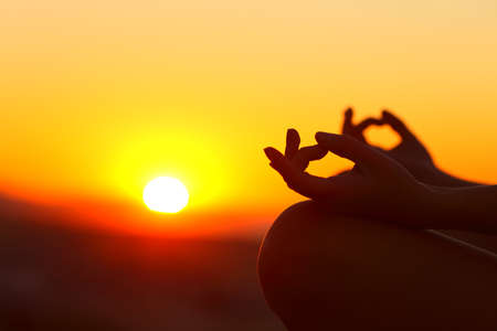 Close up of woman hands silhouette doing yoga relaxing at sunset outdoorの写真素材