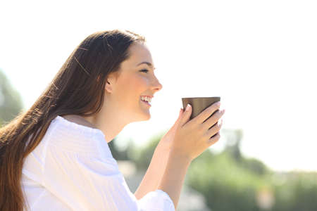 Side view of a happy woman holding a coffee cup looking away outdoors contemplating viewsの写真素材