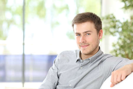 Portrait of a young man looking at camera posing sitting in the sofa at homeの写真素材