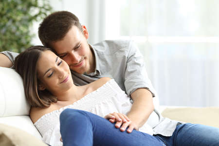 Happy couple in love cuddling holding hands sitting on the sofa in the living room at homeの写真素材