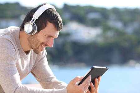 Happy man listening music with wireless headphones on a tablet sitting on the beachの写真素材