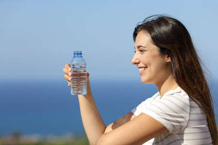 Happy woman holds bottled water in a hotel balcony on the beach on summer vacationの写真素材