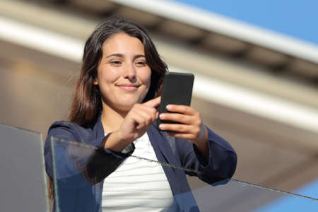 Hotel guest checking smart phone in a balcony a sunny day