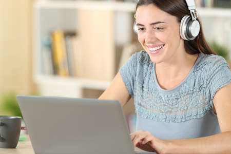 Happy student with headphones and laptop e-learning on a desk at homeの写真素材