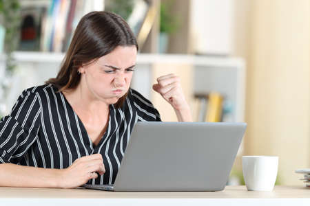 Angry woman checking laptop siting in a desk at homeの写真素材