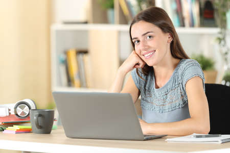 Happy student posing looking at camera sitting on a chair at homeの写真素材