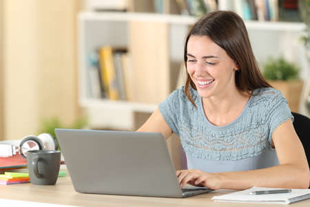 Happy student laughing using laptop e- learning sitting on a desk at homeの写真素材