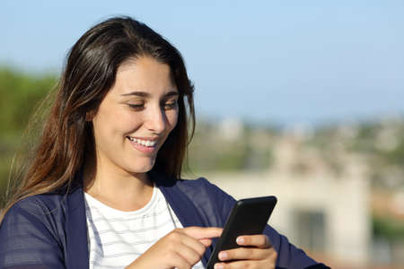Happy woman checking smart phone outdoors a sunny dayの写真素材