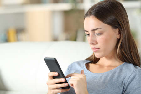Teen using smart phone sitting on a couch in the living room at homeの写真素材