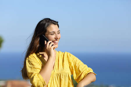 Happy woman calling on phone in a hotel balcony on the beach on summerの写真素材