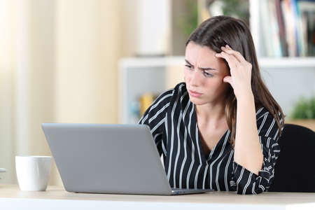 Worried woman checking laptop sitting on a chair at homeの写真素材
