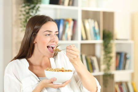 Happy girl opening mouth eating cereal for breakfast at homeの写真素材