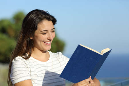 Happy woman reading a book in a hotel balcony on the beach on summer vacation