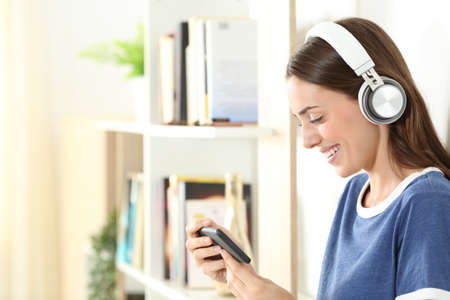 Profile of a happy teen wearing wireless headphones watching media on smart phone at homeの写真素材