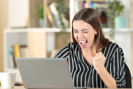 Excited woman checking good news on laptop at homeの写真素材