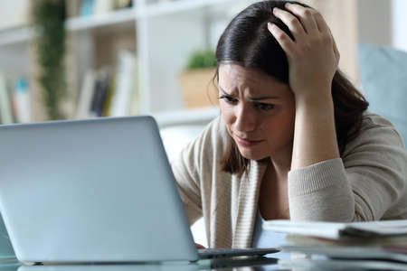 Sad woman complaining checking bad news on email email on a laptop at homeの写真素材