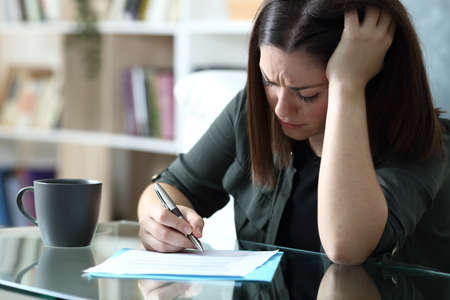 Sad woman sigining document complaining sitting in the living room at homeの写真素材