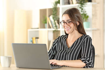Elegant woman wearing eyeglasses using laptop on a desk at homeの写真素材