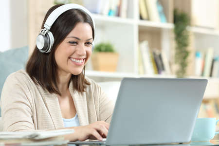 Happy woman with headphones using a laptop sitting in a desk at homeの写真素材