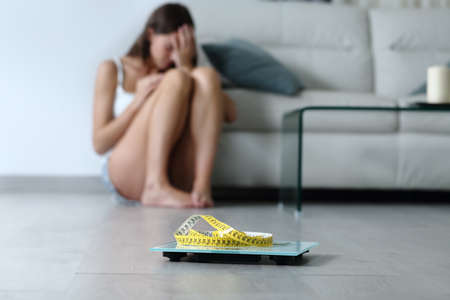 Sad teen complaining about her body weight sitting on the floor with a scale in foregroundの写真素材