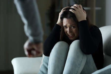 Scared woman victim of gender violence sitting on a couch in the night at homeの写真素材