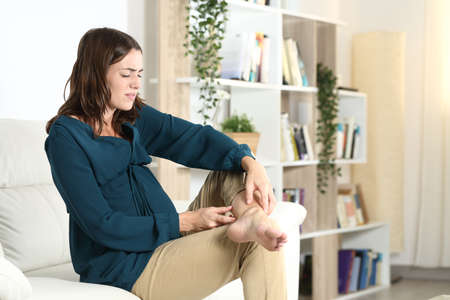 Pregnant woman suffering ankle ache complaining sitting on a sofa in the living room at homeの写真素材