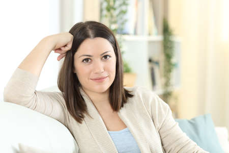 Satisfied homeowner looking at camera sitting on a couch in the living room at homeの写真素材