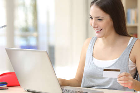 Happy student woman paying with credit card on laptop sitting on a desk at homeの写真素材