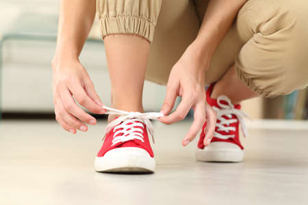 Front view close up of woman tying shoelaces of sneakers on the floor in the living room at homeの写真素材