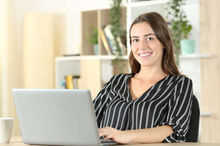 Happy woman posing looking at camera using a laptop in a desk at homeの写真素材