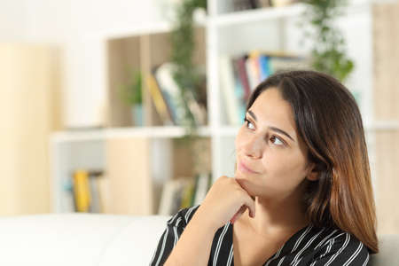 Thoughtful woman looking at side sitting on a sofa in the living room at home