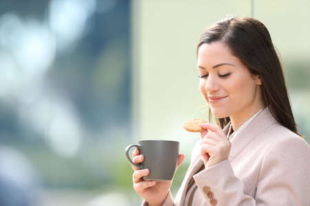 Entrepreneur eating cookie and drinking coffee at breakfast standing on the street