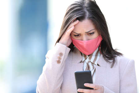 Worried businesswoman with mask reading smart phone content in coronavirus timerの写真素材