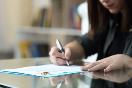 Wife signing divorce document with wedding rings over it at homeの写真素材