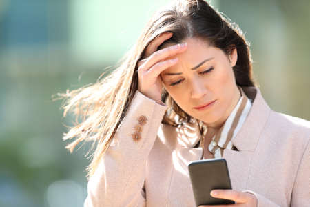 Sad entrepreneur complaining checking smart phone content in the streetの写真素材