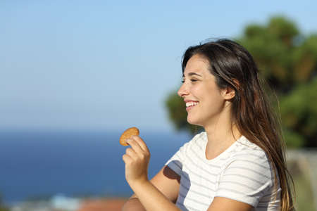Happy woman holding cookie in an apartment balcony on the beach on summer vacationの写真素材