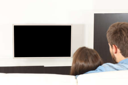 Back view of a couple cuddling watching tv with blank screen sitting in the sofa at homeの写真素材