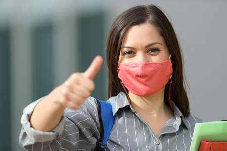 Front view portrait of a happy student wearing mask with thumbs up in the streetの写真素材