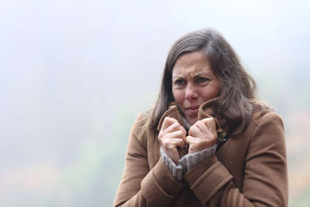 Stressed middle age woman getting cold grabbing jacket complaining in winter standing outdoors