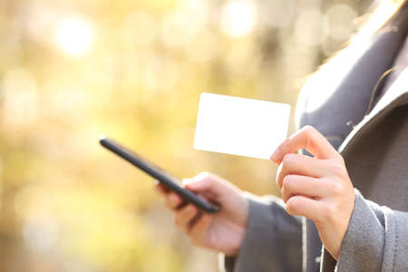 Close up profile of woman buying online with smart phone showing blank credit card in fall in a parkの写真素材