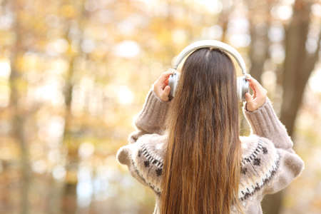 Back view portrait of woman putting headphones in autumn in a parkの写真素材