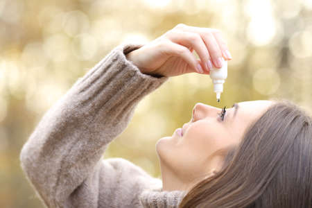 Close up of a woman with dry eyes applying artificial tear in winter in a parkの写真素材